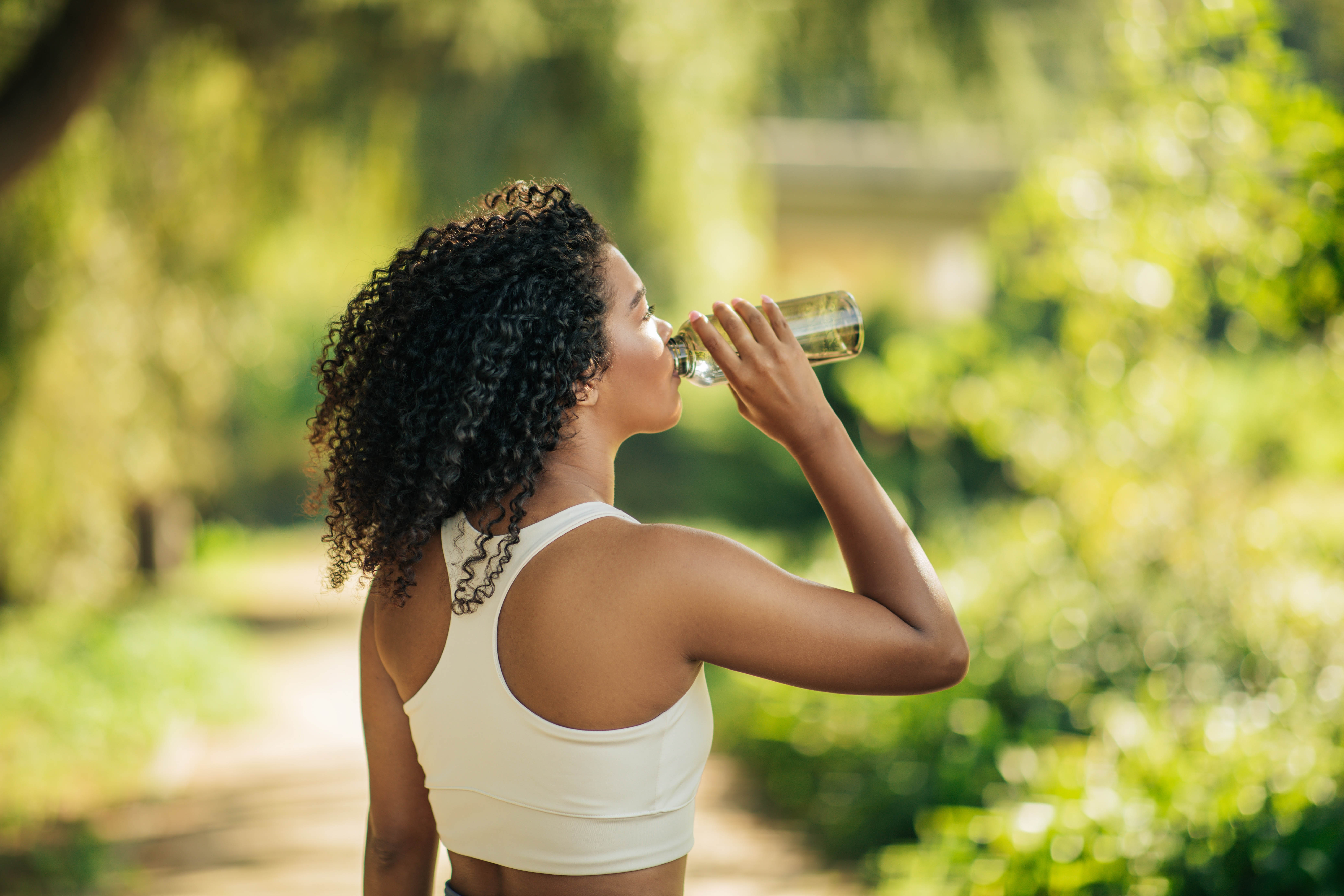 Young woman outside drinking from her glass water bottle Young woman outside drinking from her glass water bottle
